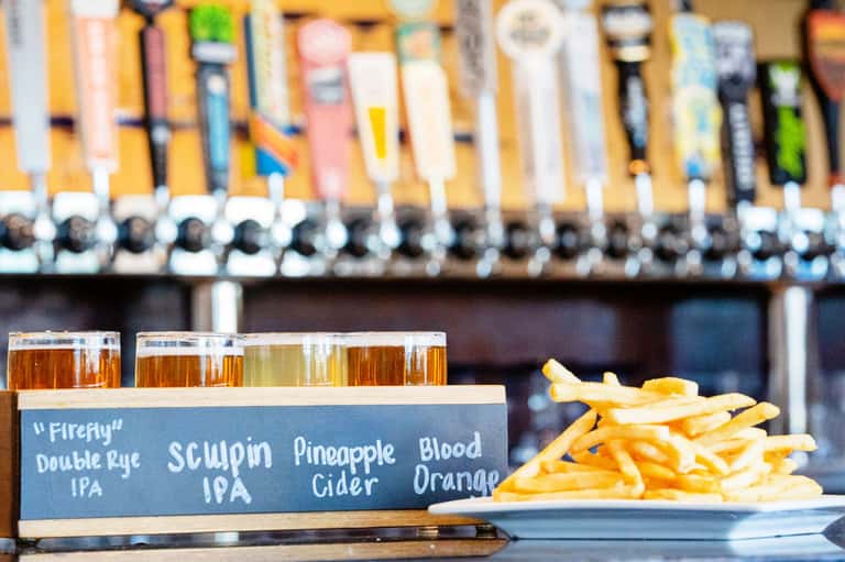 Beer flight and French fries on bar counter with tap handles in background