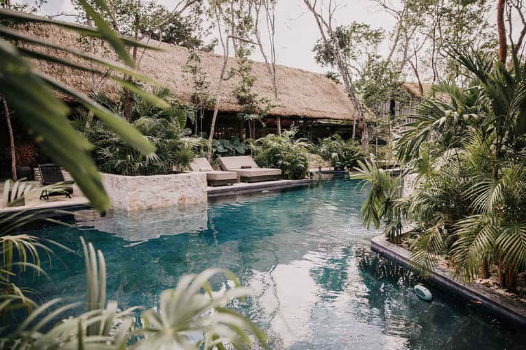 Tropical pool surrounded by thatched-roof structures and lush jungle vegetation