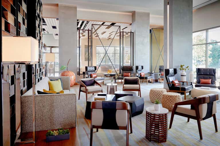 Modern hotel lobby with contemporary furniture, warm wood tones, and large windows with natural light