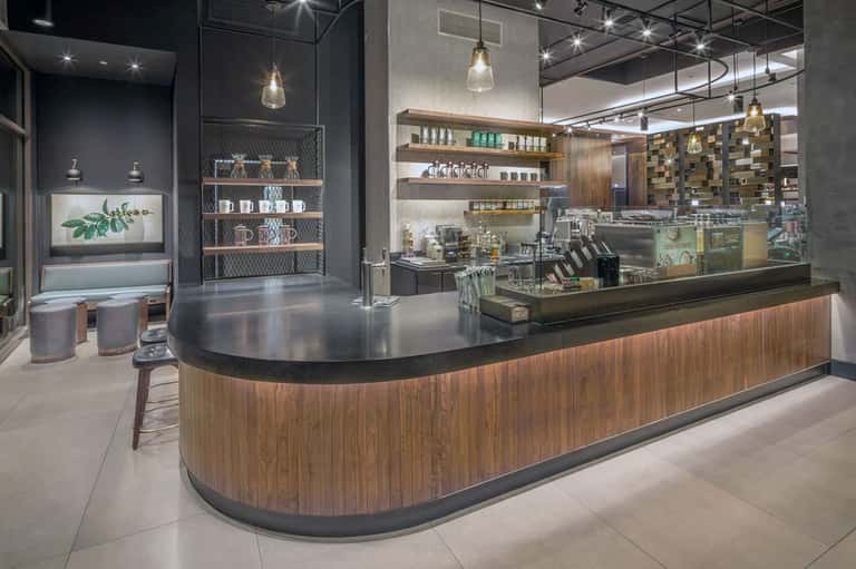 Modern spa reception area with curved wood counter, shelving, pendant lights, and botanical decor
