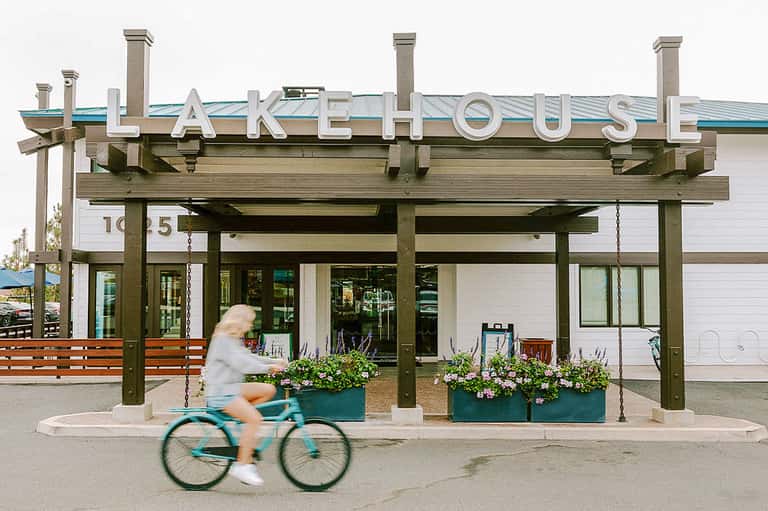 Lake House storefront with wooden pergola, white building, blue roof, and person on bicycle