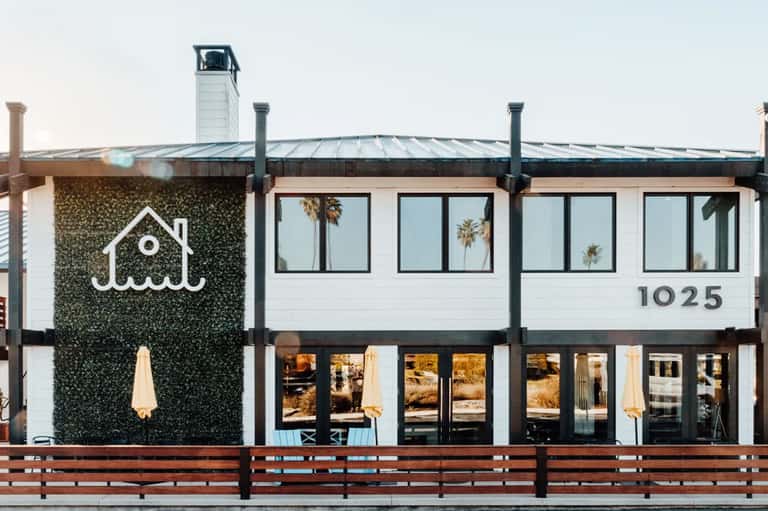 Modern beachfront restaurant building with ivy walls and palm tree reflections