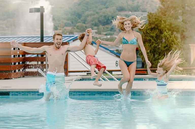 Family playing and splashing in resort pool with mountain valley views in background