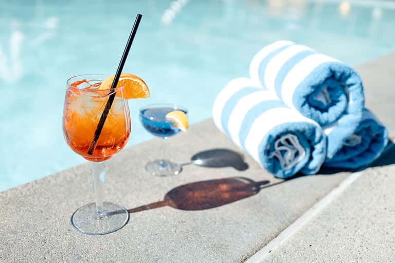 Cocktail with orange slice on pool deck beside rolled blue and white striped towels