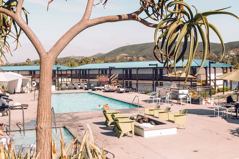 Resort pool area with fire pit, loungers, and scenic lake and mountain backdrop
