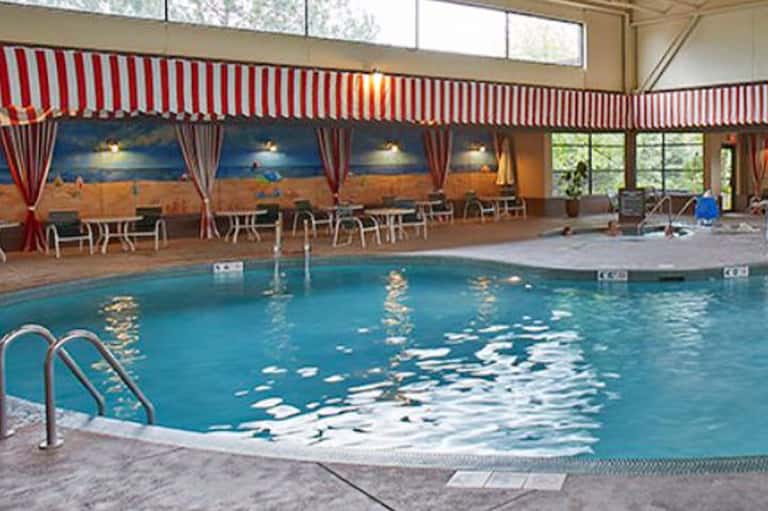 Indoor swimming pool with red and white striped awning, beach mural, lounge chairs, and natural light from windows