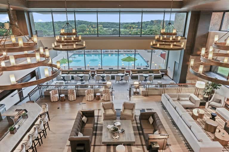 Modern resort atrium lounge with hanging chandeliers, indoor pool, and lush greenery