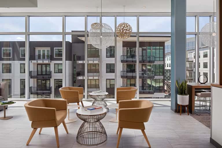 Modern lounge area with tan seating, hanging pendant lights, and floor-to-ceiling windows