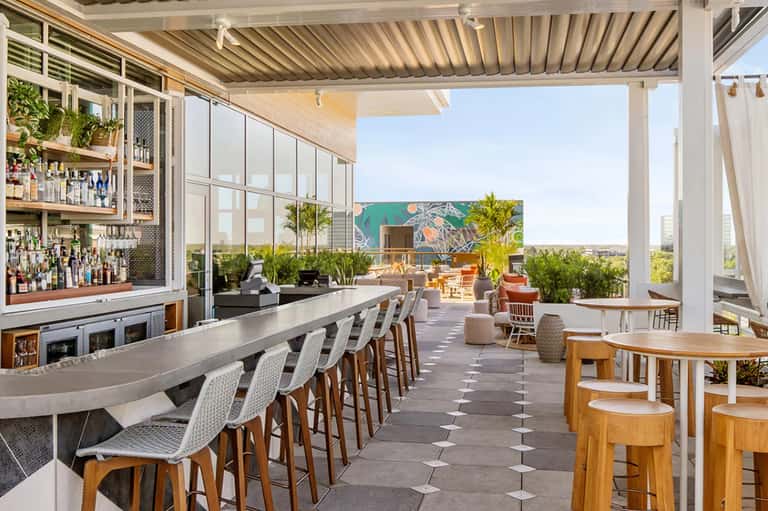 Rooftop bar with curved counter, floor-to-ceiling windows, and panoramic desert landscape views