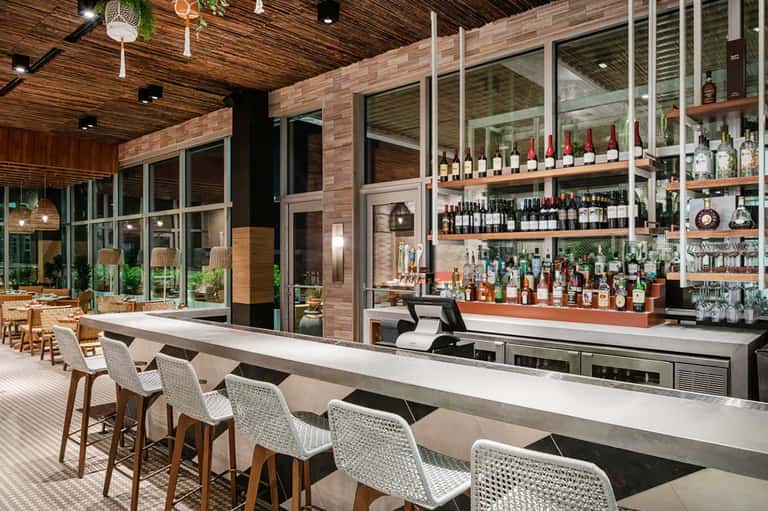 Modern outdoor bar with wooden ceiling, wine shelves, and white barstool seating