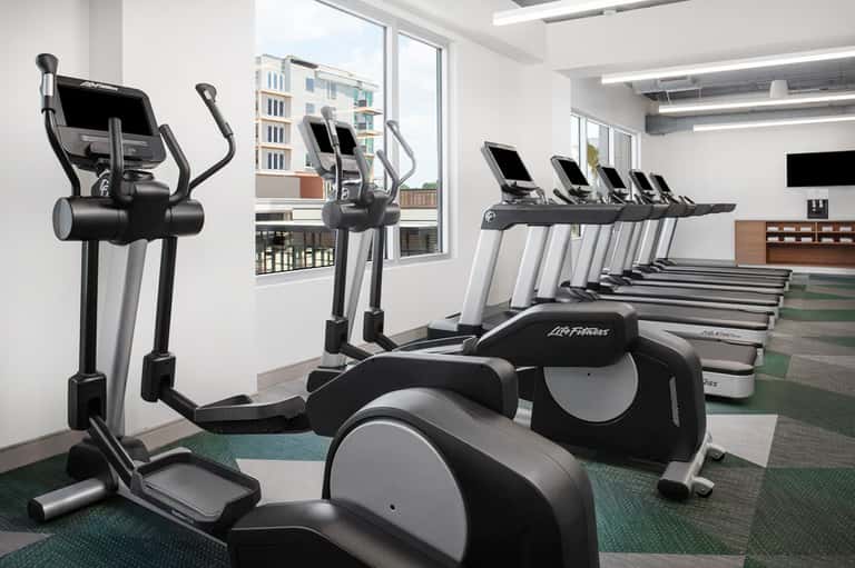 Modern hotel fitness center with elliptical machines, treadmills, large windows overlooking city buildings