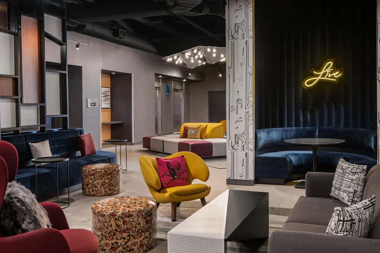 Modern hotel lounge with blue velvet seating, colorful accent chairs, neon sign and contemporary decor