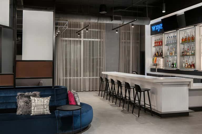 Contemporary hotel bar with blue velvet seating, full liquor shelves, and lounge area