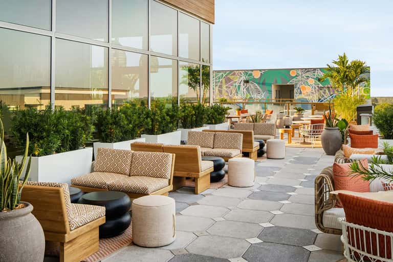 Contemporary rooftop lounge with wooden seating, colorful mural backdrop, native plants, and panoramic views