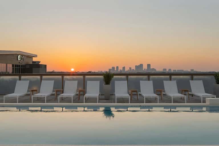 Rooftop pool overlooking city skyline at sunset with white lounge chairs
