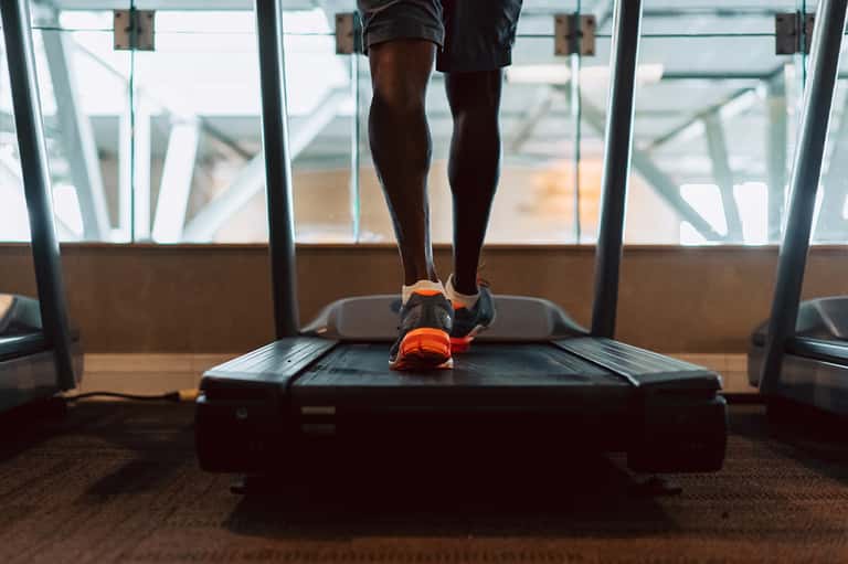 Person running on treadmill in gym with floor-to-ceiling windows overlooking beach