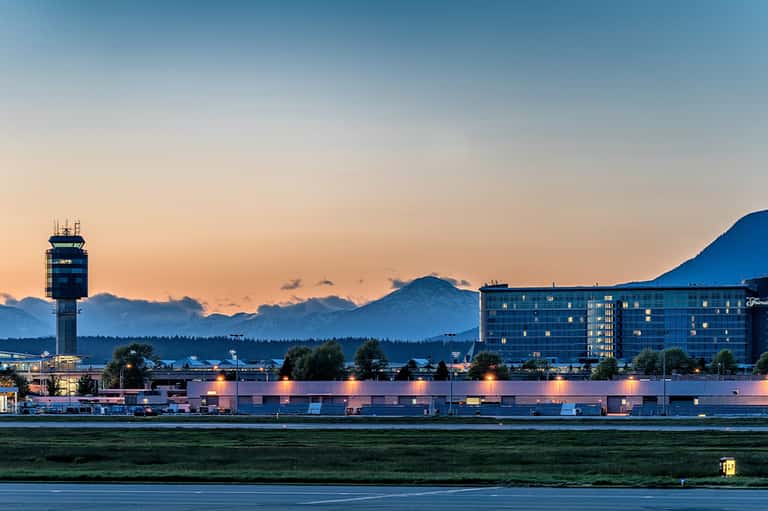 Hotel exterior at dusk with illuminated building, mountains, and control tower backdrop