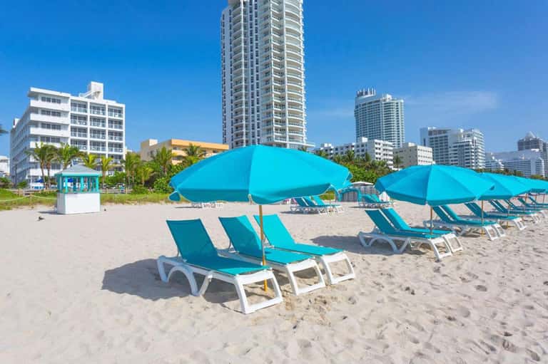Miami beach with bright turquoise umbrellas and loungers facing high-rise hotels