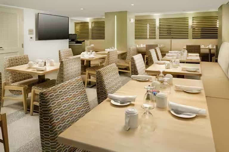 Formal dining room with patterned chairs, wooden tables, place settings, TV screen, and green accents