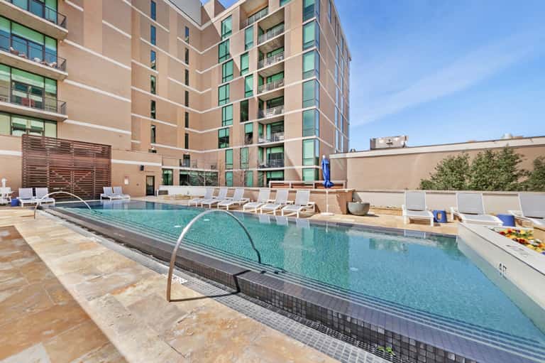 Urban hotel courtyard pool with turquoise water, white lounge chairs, and multi-story brick building backdrop