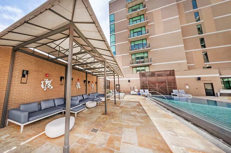 Urban rooftop pool area with modern lounging space, metal shade structures, and city building backdrop
