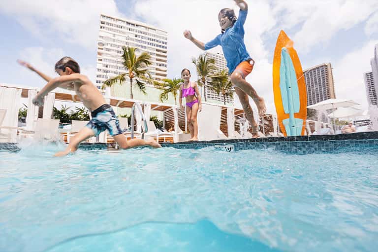 Children playing and jumping in pool at resort with high-rise buildings in background