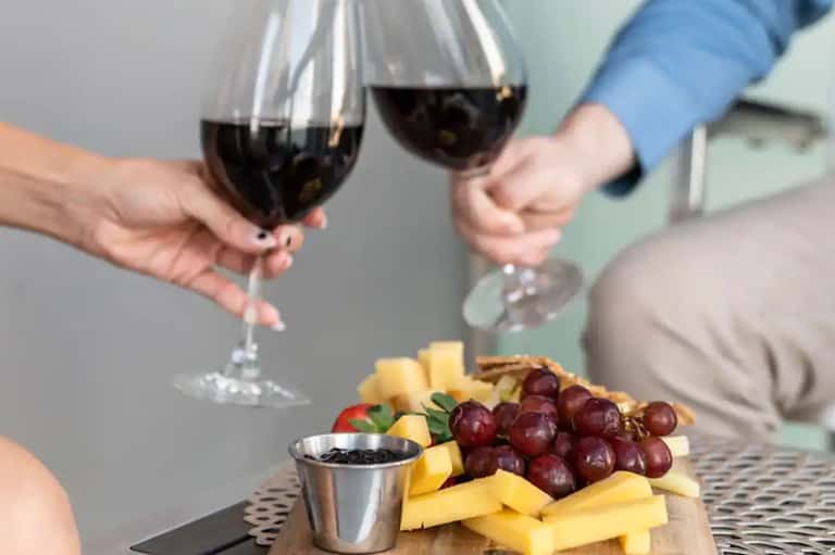 Two people toasting with wine glasses near a cheese and grape platter