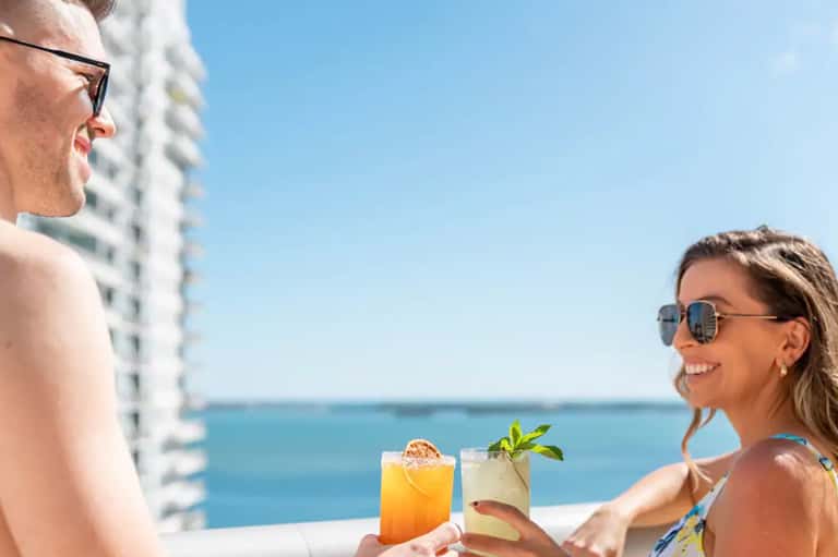 Couple enjoying tropical cocktails on oceanview balcony with high-rise building
