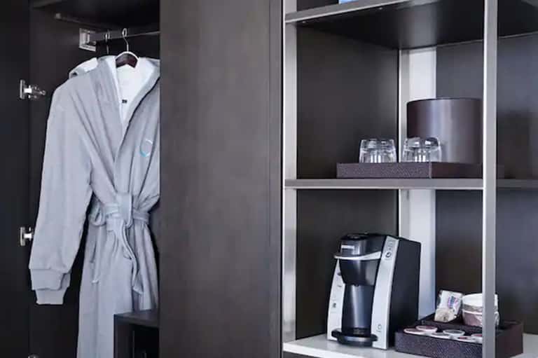 Hotel room amenities including white robe and welcome items in dark cabinet