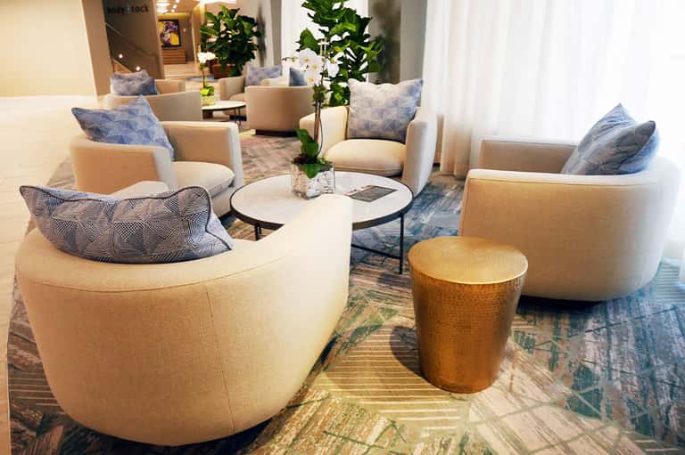 Contemporary hotel lobby lounge with cream-colored curved chairs, blue patterned pillows, and plants