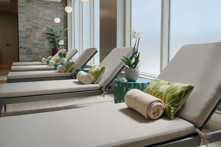 Spa relaxation area with multiple cushioned loungers, towel rolls, and ocean view windows