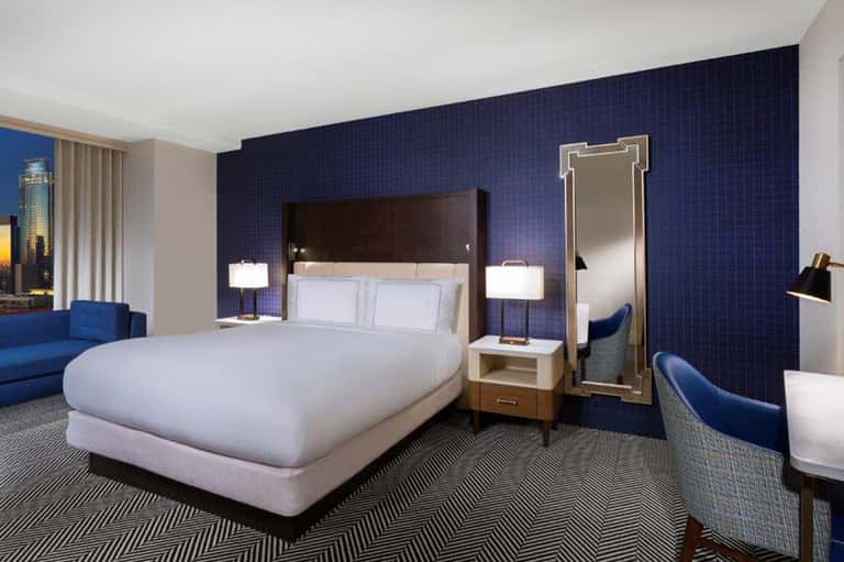 Hotel bedroom with navy accent wall, king bed, blue seating, and city views through windows