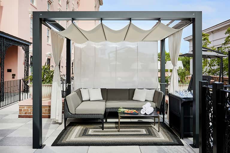 Black pergola with white draped curtains and comfortable seating area