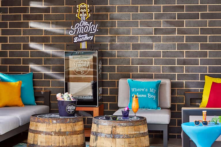 Modern lounge area with colorful pillows, brick wall, barrel tables, and distillery sign