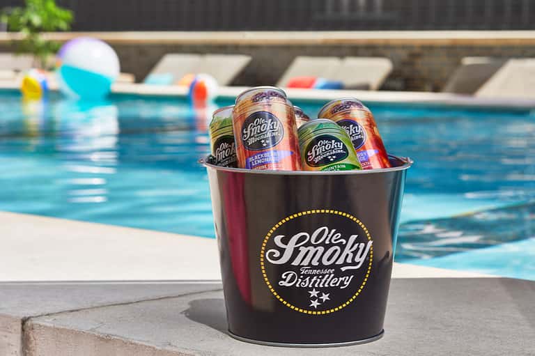 Ole Smoky whiskey bucket with cans poolside at resort with lounge chairs and blue water
