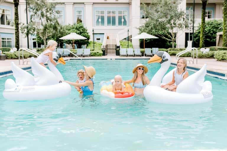 Family enjoying pool with giant swan floats and lounge chairs on white deck