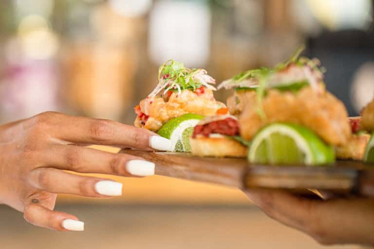 Chef presenting appetizers with lime garnish and microgreens on wooden board