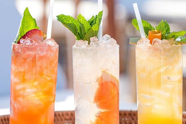 Three colorful refreshing beverages with citrus slices and fresh mint on white surface