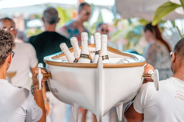 Champagne bottle bucket at outdoor event with attendees in white attire celebrating