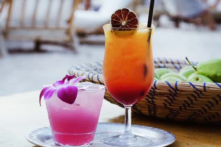 Two tropical cocktails on a table with orchid flower and ocean view behind