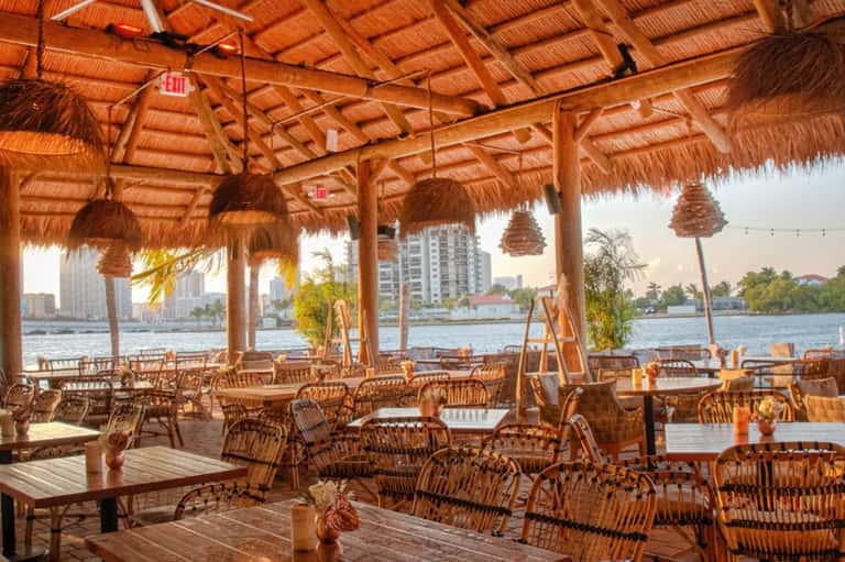 Covered beachside dining area with woven chairs and ocean waterfront views