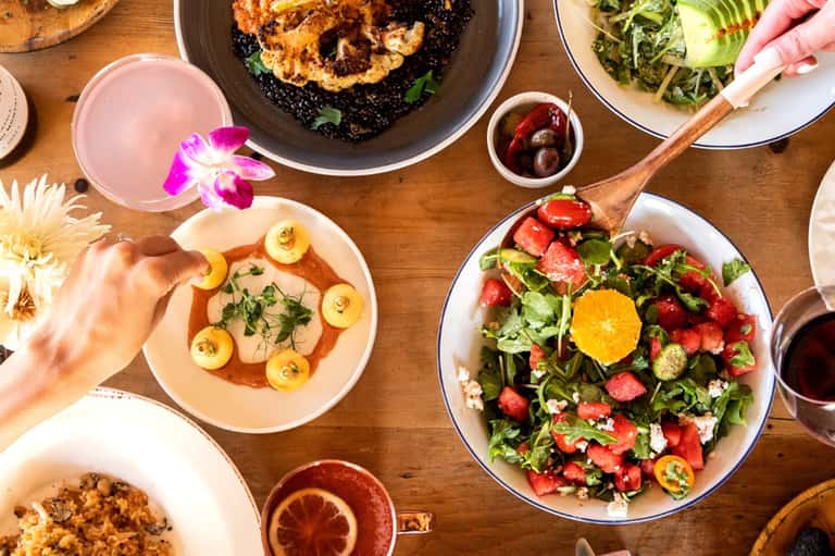 Overhead view of colorful gourmet dishes with fresh salad and flowers on table