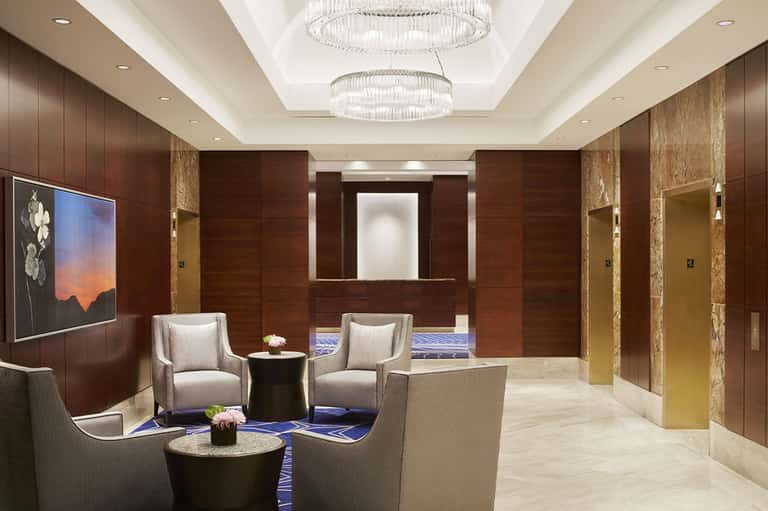 Luxury hotel elevator lobby with wood paneling, elegant seating, and crystal chandeliers