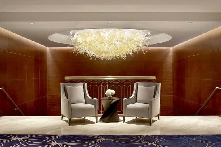 Modern hotel lobby with sophisticated seating area, feathered ceiling fixture, and warm lighting