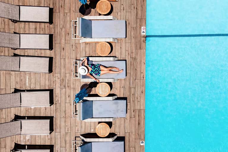 Aerial view of swimming pool deck with lounge chairs and sunbathers on wooden platform