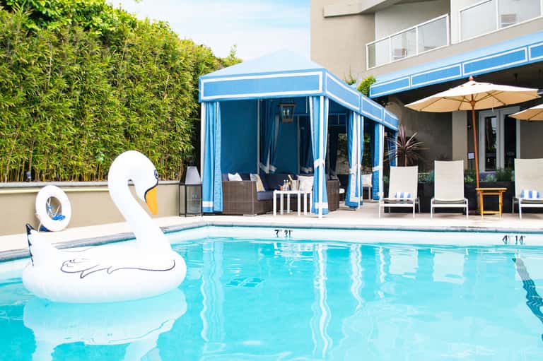 Resort swimming pool with white swan float, blue cabana, lounge chairs, and bamboo hedge backdrop