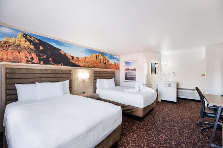 Hotel room with two queen beds and desert landscape artwork above headboards