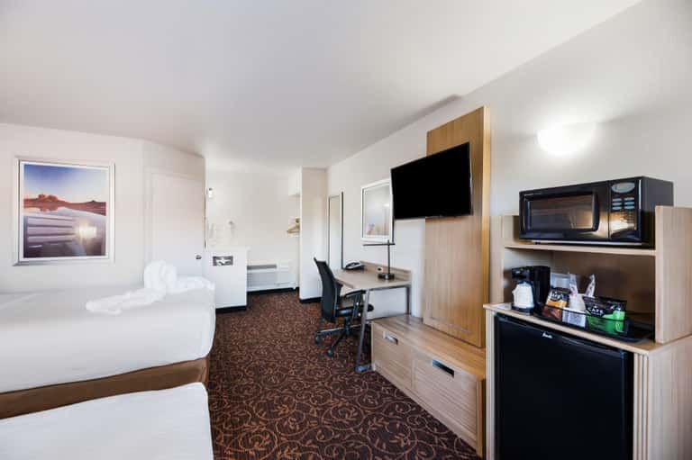 Hotel room with two queen beds, desk with TV, microwave, and brown patterned carpet