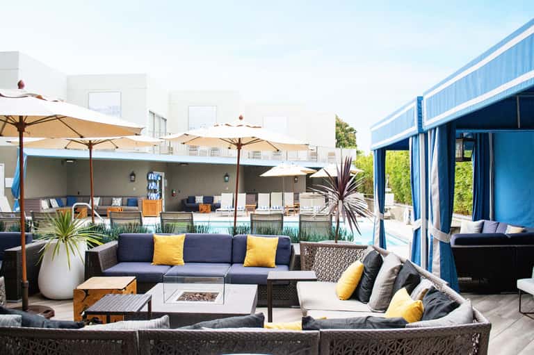 Modern resort courtyard with lounge seating, umbrellas, pool, and blue architecture