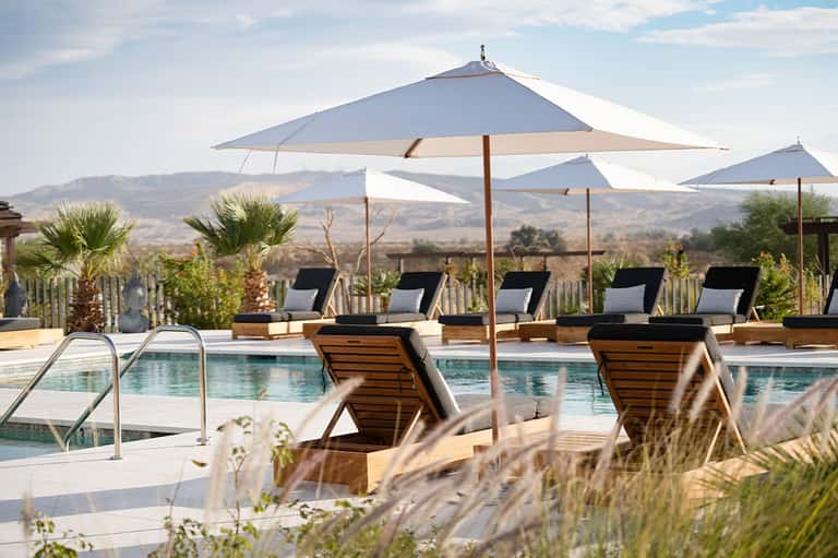 Resort pool with lounge chairs, white umbrellas, and mountain landscape in background
